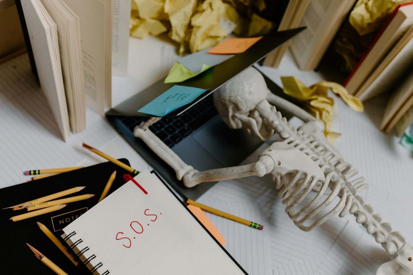 Dramatic still life of a skeleton overwhelmed at an untidy office desk with S.O.S. note.